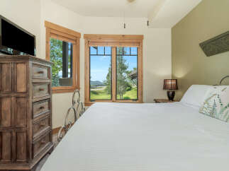 Experience breathtaking mountain views from this charming bedroom, featuring a comfortable king-size bed and a large dresser with a mounted TV.