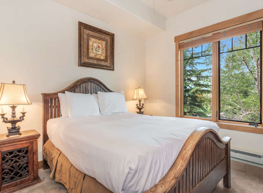 Experience serene mountain living in this charming bedroom, featuring a rustic wooden bed frame and a large window offering picturesque views of lush green trees.