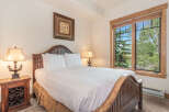 Experience serene mountain living in this charming bedroom, featuring a rustic wooden bed frame and a large window offering picturesque views of lush green trees.