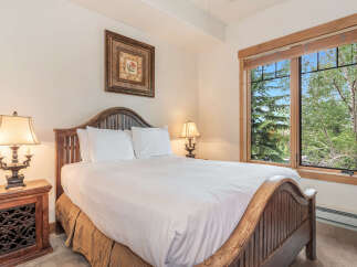 Experience serene mountain living in this charming bedroom, featuring a rustic wooden bed frame and a large window offering picturesque views of lush green trees.