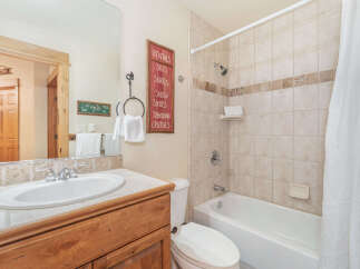 This charming bathroom features a spacious vanity with a white sink and chrome fixtures, complemented by a large mirror reflecting the wooden door and a decorative sign.