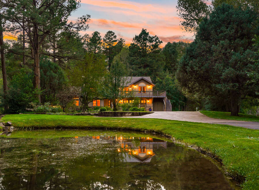 Nestled amidst lush greenery and mature trees, this stunning property offers a serene retreat with a picturesque pond reflecting the warm glow of the house.