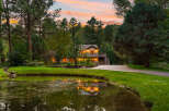 Nestled amidst lush greenery and mature trees, this stunning property offers a serene retreat with a picturesque pond reflecting the warm glow of the house.