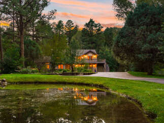 Nestled amidst lush greenery and mature trees, this stunning property offers a serene retreat with a picturesque pond reflecting the warm glow of the house.
