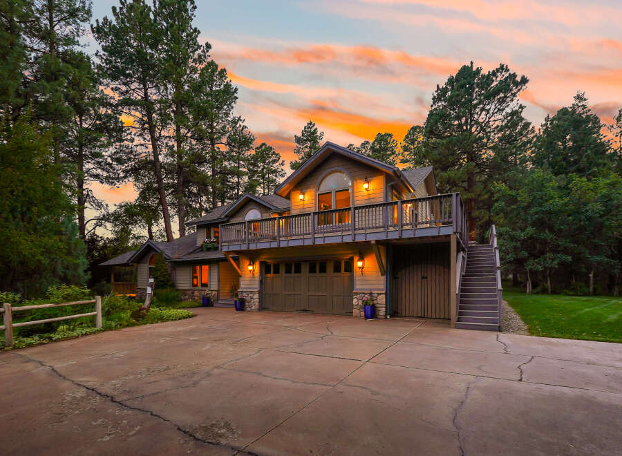Nestled amidst tall pine trees, this stunning multi-level home offers a picturesque setting with a vibrant sunset sky.