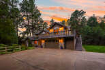 Nestled amidst tall pine trees, this stunning multi-level home offers a picturesque setting with a vibrant sunset sky.