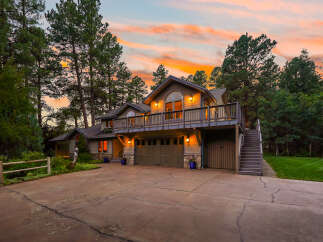 Nestled amidst tall pine trees, this stunning multi-level home offers a picturesque setting with a vibrant sunset sky.