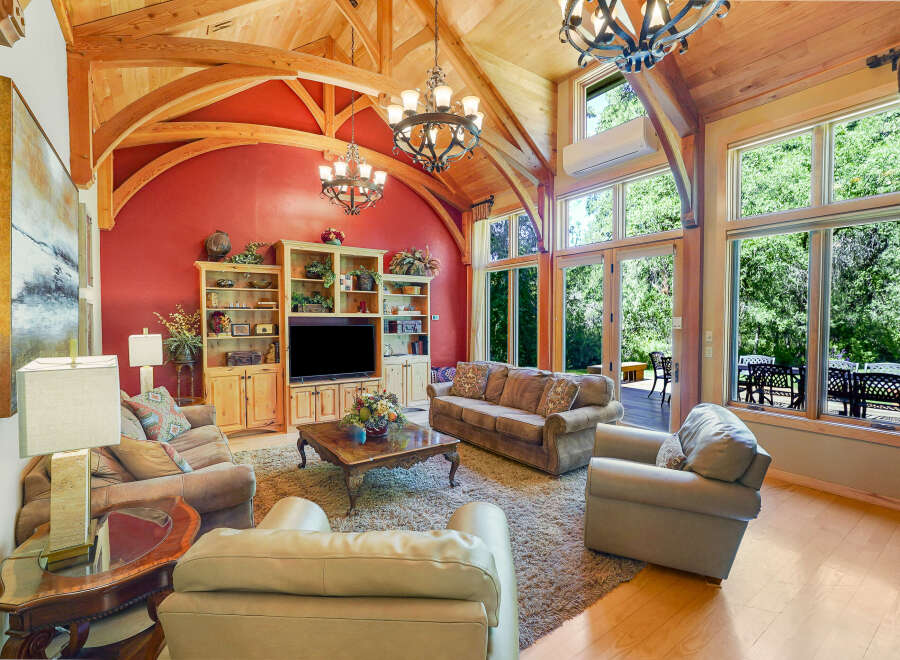 Experience luxurious living in this stunning great room, featuring a vaulted wood-beam ceiling and a vibrant red accent wall.