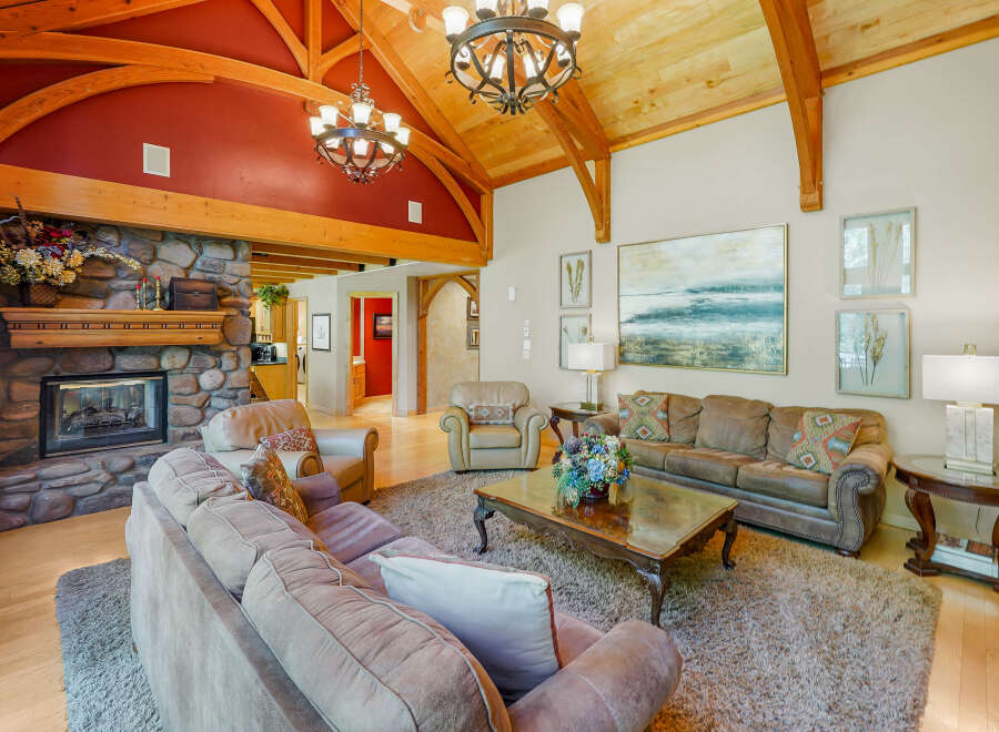 Experience rustic elegance in this spacious living room, featuring a grand stone fireplace and soaring vaulted ceilings with exposed wooden beams.