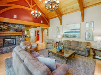 Experience rustic elegance in this spacious living room, featuring a grand stone fireplace and soaring vaulted ceilings with exposed wooden beams.