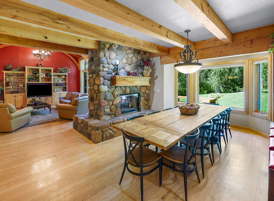 Experience rustic charm in this spacious living and dining area, featuring a grand stone fireplace and exposed wooden beams.