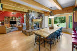 Experience rustic charm in this spacious living and dining area, featuring a grand stone fireplace and exposed wooden beams.