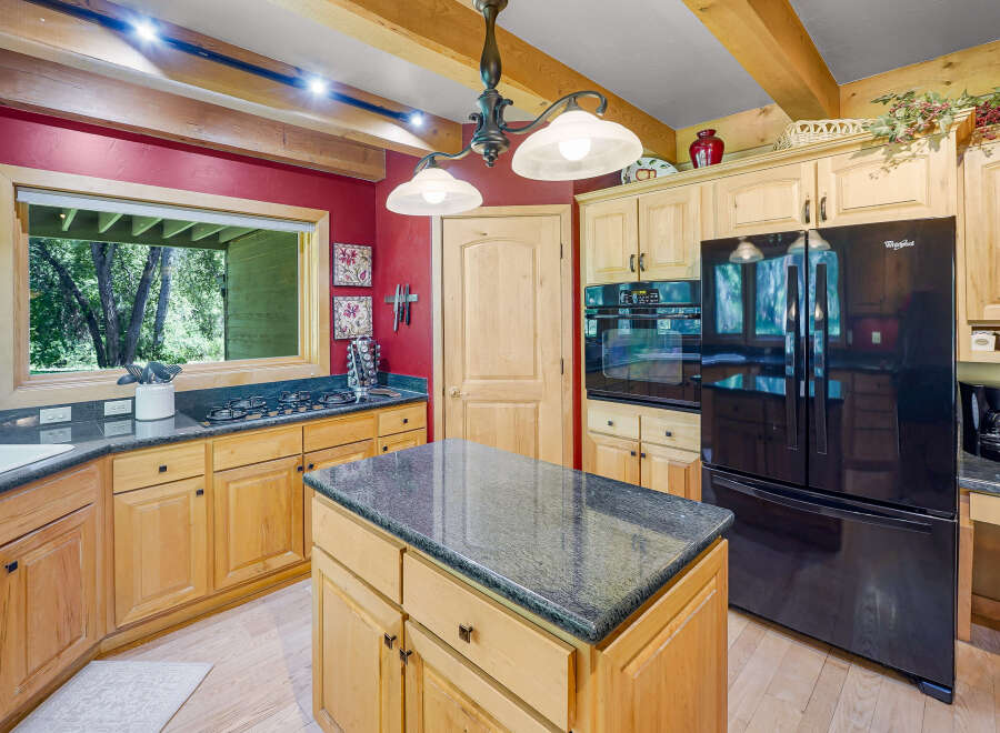 This spacious kitchen features warm, light wood cabinetry complemented by a striking red accent wall and exposed wooden beams.