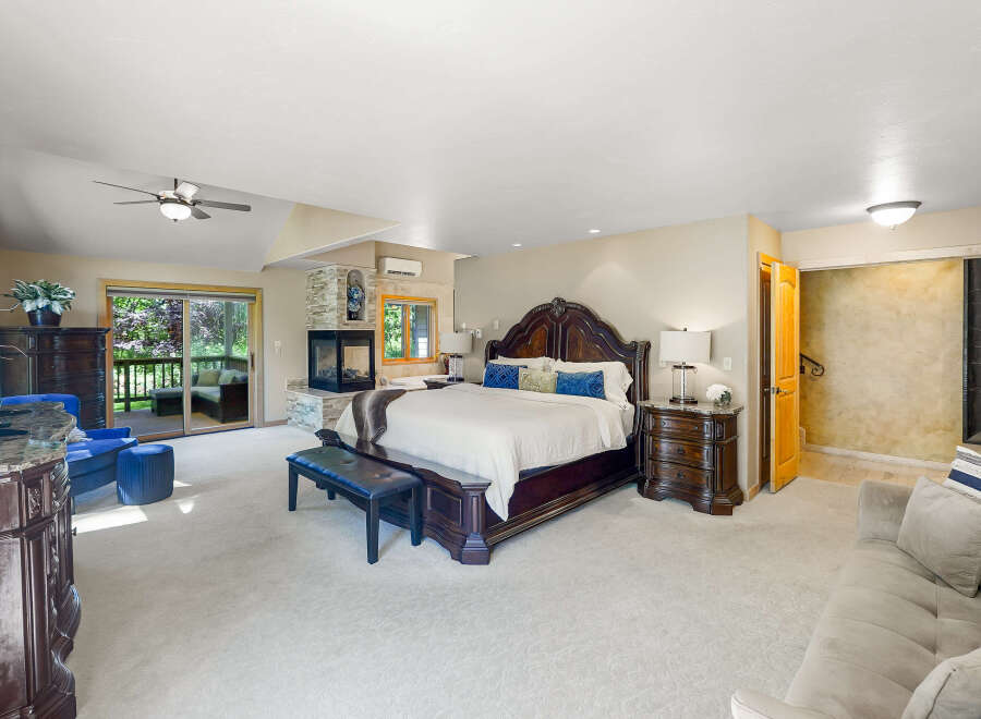 Experience luxurious living in this spacious master suite, featuring a cozy fireplace and direct access to an outdoor patio, perfect for enjoying the surrounding nature.