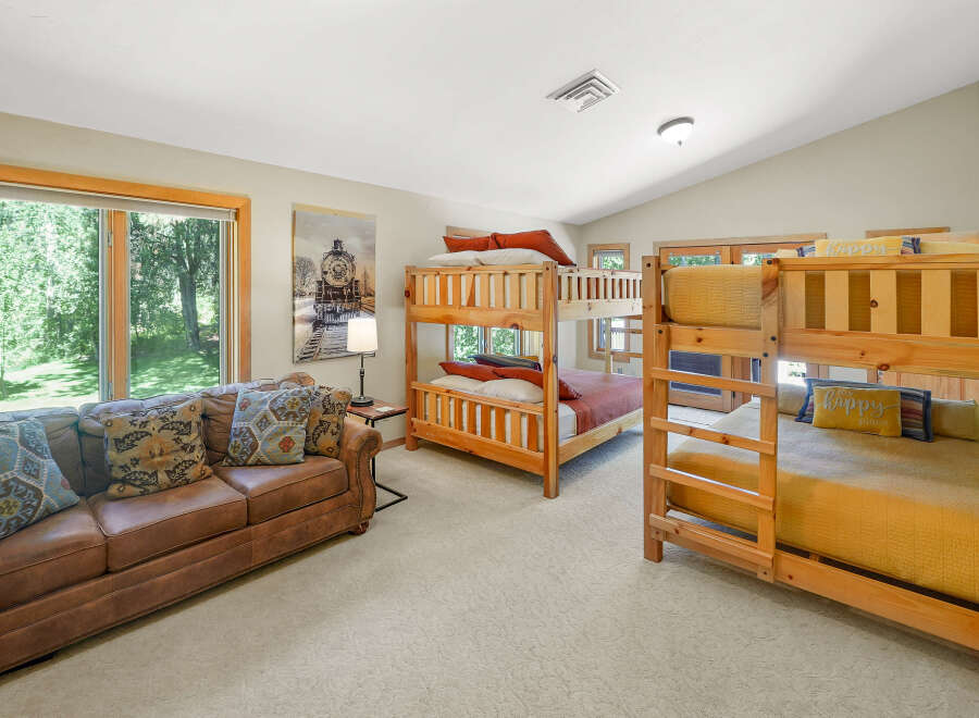 This spacious bedroom is perfect for families or groups, featuring two sets of sturdy wooden bunk beds and a comfortable leather sofa.