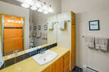 This vibrant bathroom features a striking orange tiled shower with a glass door, complemented by a sunny yellow tiled countertop and backsplash.