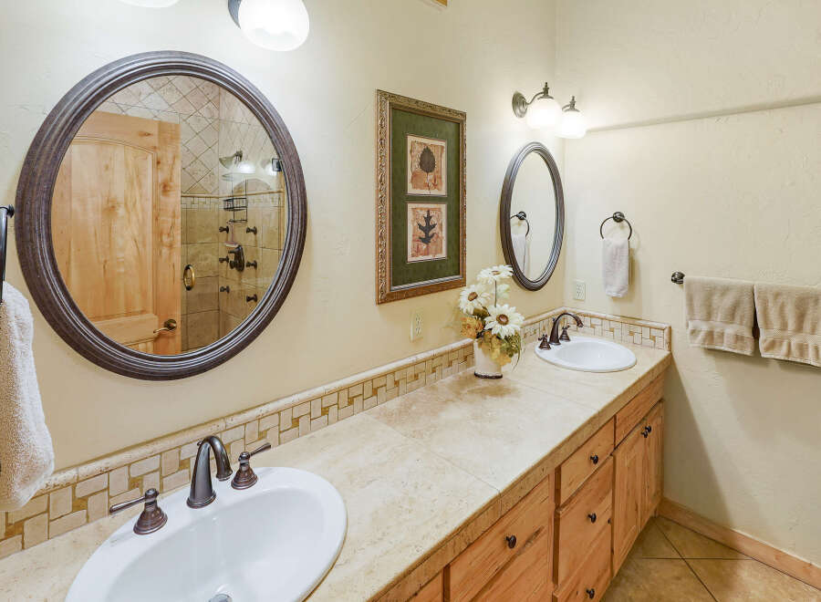 This charming bathroom features a dual vanity with a tiled backsplash and a large oval mirror reflecting a wooden door and shower.