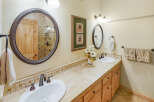 This charming bathroom features a dual vanity with a tiled backsplash and a large oval mirror reflecting a wooden door and shower.