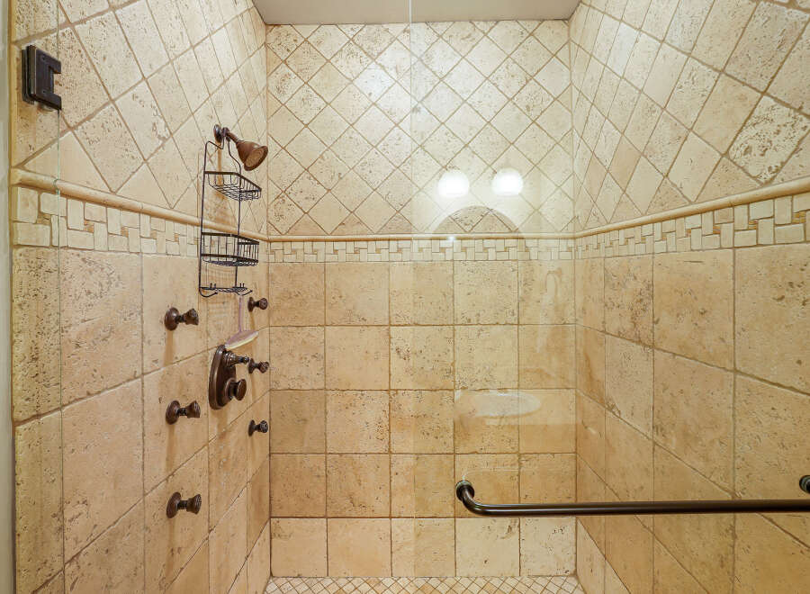 Experience luxury in this spacious walk-in shower, featuring elegant travertine tile and a multi-head shower system for a spa-like experience.