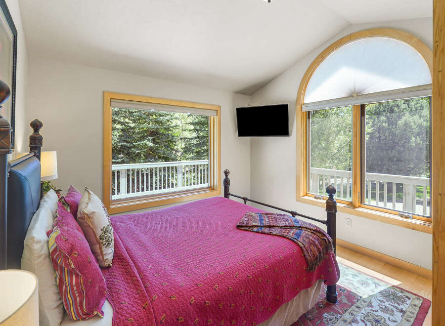 Experience serene mountain living in this charming bedroom, featuring a comfortable queen-size bed adorned with a vibrant pink quilt and decorative pillows.