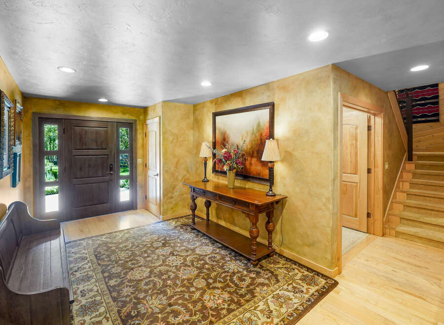 Step into this inviting entryway featuring a rustic wooden bench and a large, ornate rug that complements the warm, textured walls.