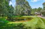 Discover this stunning property featuring a serene pond surrounded by lush greenery and mature trees, offering a tranquil oasis.