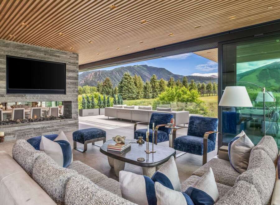 Experience luxurious indoor-outdoor living in this stunning mountain retreat, featuring a modern living area with a stone fireplace and a large television.
