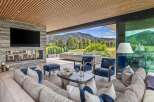 Experience luxurious indoor-outdoor living in this stunning mountain retreat, featuring a modern living area with a stone fireplace and a large television.