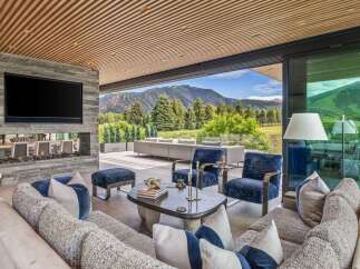 Experience luxurious indoor-outdoor living in this stunning mountain retreat, featuring a modern living area with a stone fireplace and a large television.
