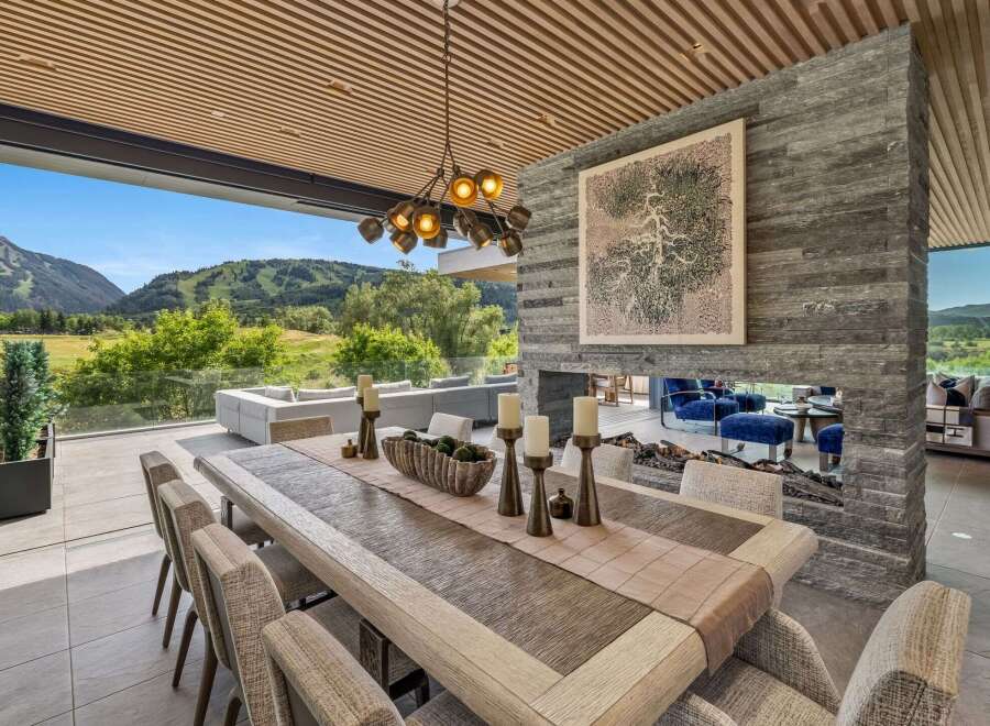 Experience luxurious indoor-outdoor living with this stunning dining area, featuring a large wooden table set for a feast.