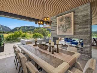 Experience luxurious indoor-outdoor living with this stunning dining area, featuring a large wooden table set for a feast.