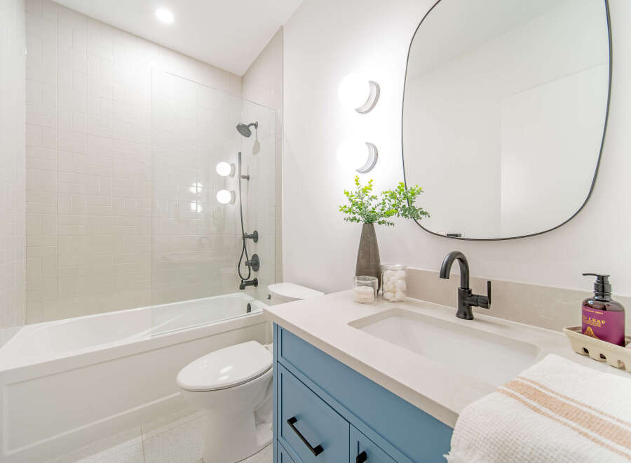 This modern bathroom features a sleek white subway tile shower and tub combination, complemented by a stylish blue vanity with black hardware.