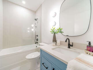 This modern bathroom features a sleek white subway tile shower and tub combination, complemented by a stylish blue vanity with black hardware.