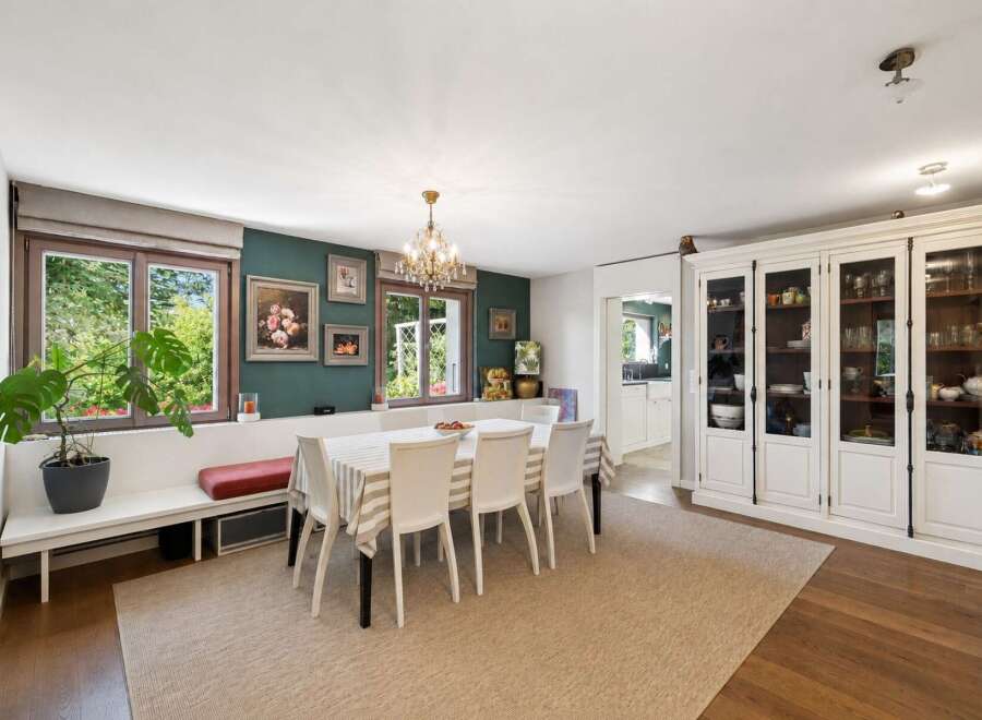 This elegant dining room features a built-in bench seating area with a red cushion, complemented by a striped tablecloth and white chairs around a dining table.