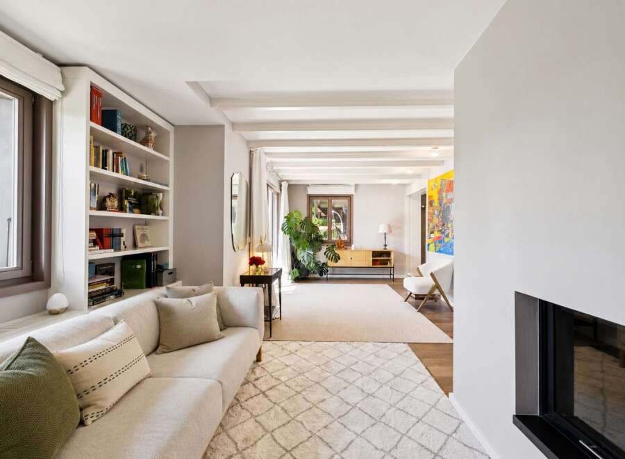 This spacious living room features a comfortable sectional sofa, a built-in bookshelf filled with decorative items and books, and a large window offering natural light.