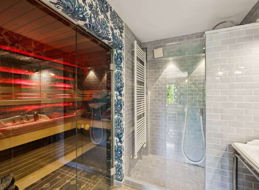 Experience ultimate relaxation in this luxurious bathroom featuring a modern sauna with vibrant red lighting and a spacious walk-in shower.
