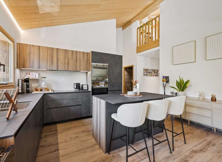 Experience modern living in this stunning kitchen featuring sleek, dark cabinetry complemented by warm wood accents on the upper cabinets and island.
