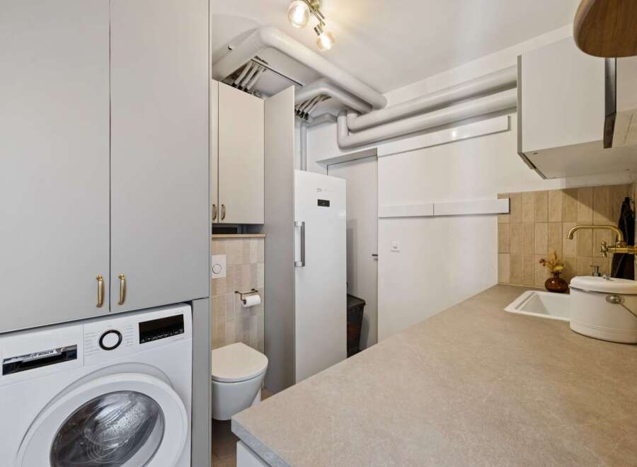 Discover this compact and functional utility room, featuring a modern Bosch washing machine and ample storage cabinets.