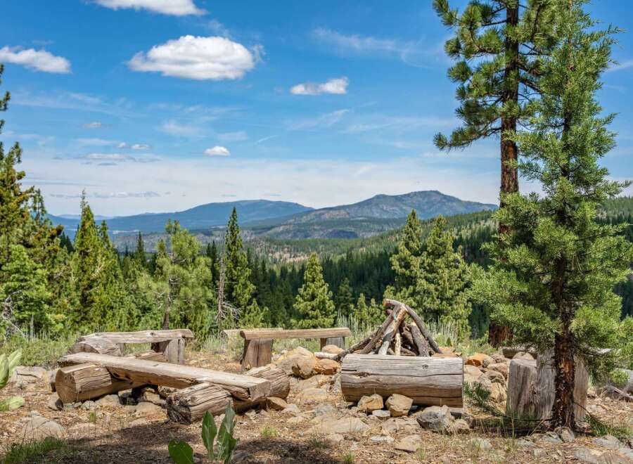 Experience the ultimate mountain getaway with this rustic campsite, featuring log benches and a fire pit perfect for gathering.