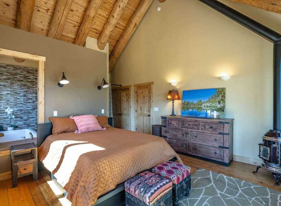 Experience rustic charm in this unique bedroom featuring a vaulted wood-beamed ceiling and a cozy wood-burning stove.