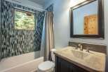 This modern bathroom features a striking mosaic tile accent wall surrounding the bathtub and shower area, complemented by a sleek window offering natural light and scenic views.