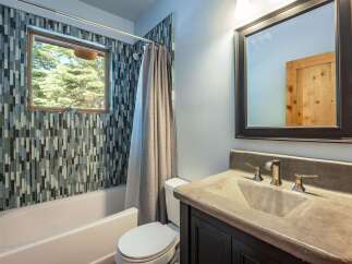 This modern bathroom features a striking mosaic tile accent wall surrounding the bathtub and shower area, complemented by a sleek window offering natural light and scenic views.