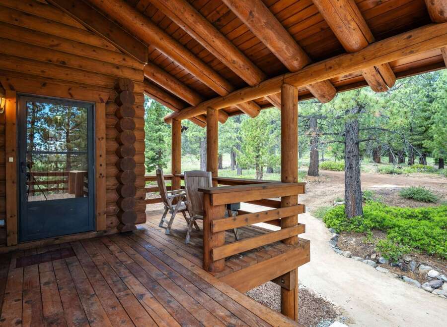 Experience rustic charm with this inviting log cabin porch, featuring a covered wooden deck perfect for enjoying the surrounding pine forest.
