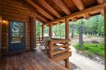 Experience rustic charm with this inviting log cabin porch, featuring a covered wooden deck perfect for enjoying the surrounding pine forest.