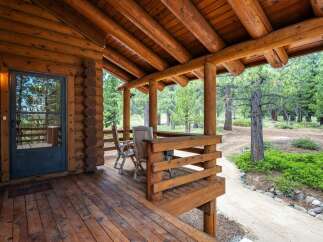 Experience rustic charm with this inviting log cabin porch, featuring a covered wooden deck perfect for enjoying the surrounding pine forest.