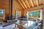 Experience rustic charm in this stunning log cabin living room, featuring a cozy fireplace and breathtaking mountain views through expansive windows.