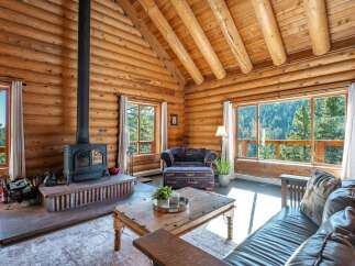 Experience rustic charm in this stunning log cabin living room, featuring a cozy fireplace and breathtaking mountain views through expansive windows.