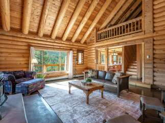 Experience rustic charm in this stunning log cabin living room, featuring a vaulted wood-beamed ceiling and a large picture window with breathtaking mountain views.