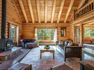 Experience rustic charm in this stunning log cabin living room, featuring a grand stone fireplace and exposed wooden beams.