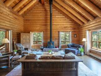 Experience rustic charm in this stunning log cabin living room, featuring a grand stone fireplace as the centerpiece.